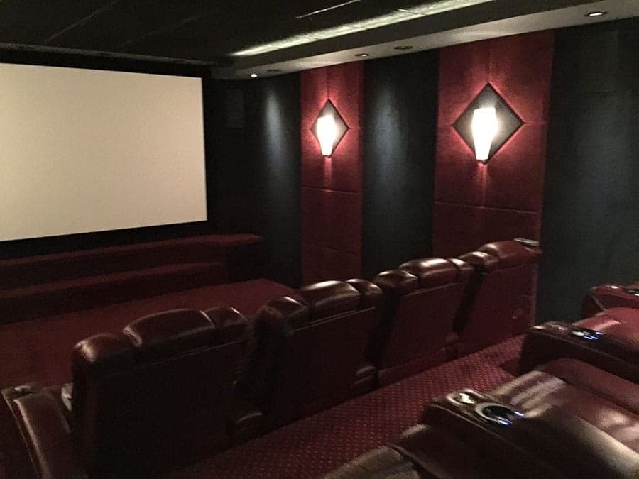 Home theater with red acoustic wall panels, sconce lighting and leather recliners